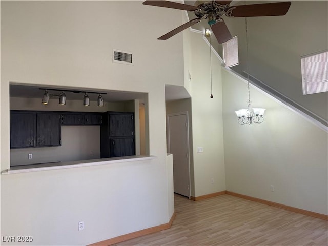 kitchen with ceiling fan with notable chandelier, a towering ceiling, hardwood / wood-style floors, and pendant lighting