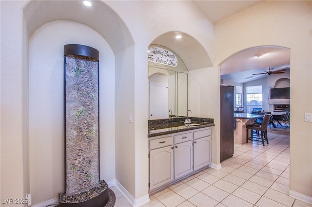 interior space with sink, ceiling fan, light tile patterned floors, white cabinets, and black fridge