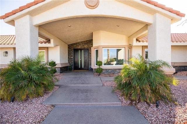 view of exterior entry featuring stone siding, a tile roof, and stucco siding