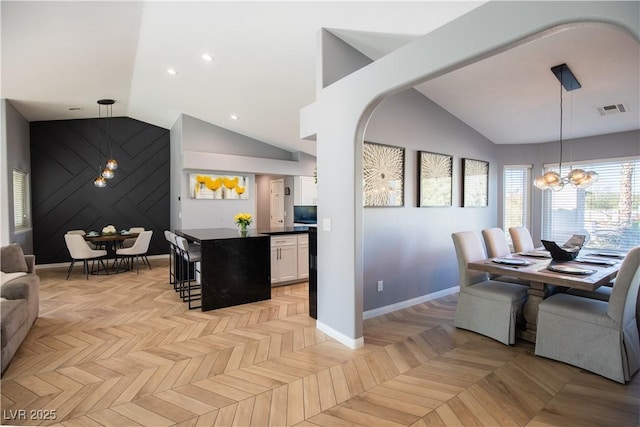 dining space with an accent wall, visible vents, baseboards, vaulted ceiling, and an inviting chandelier