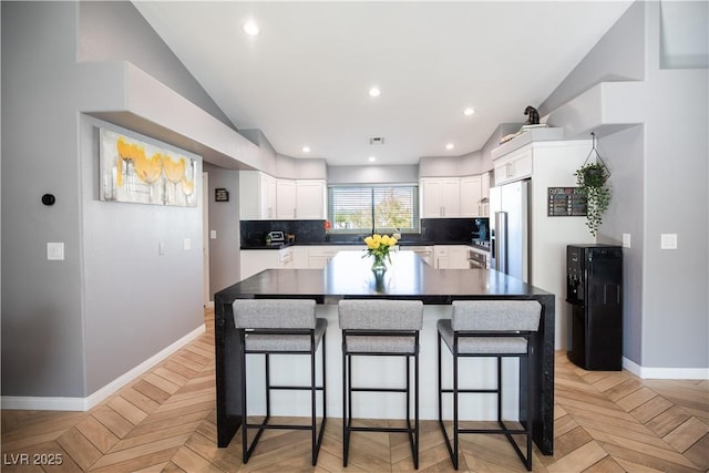 kitchen with a center island, tasteful backsplash, high end fridge, white cabinetry, and a kitchen breakfast bar