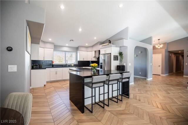 kitchen featuring stainless steel refrigerator with ice dispenser, dark countertops, decorative backsplash, a sink, and a kitchen bar