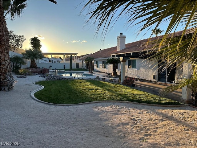 back of house at dusk featuring a chimney, fence, an outdoor pool, and a lawn