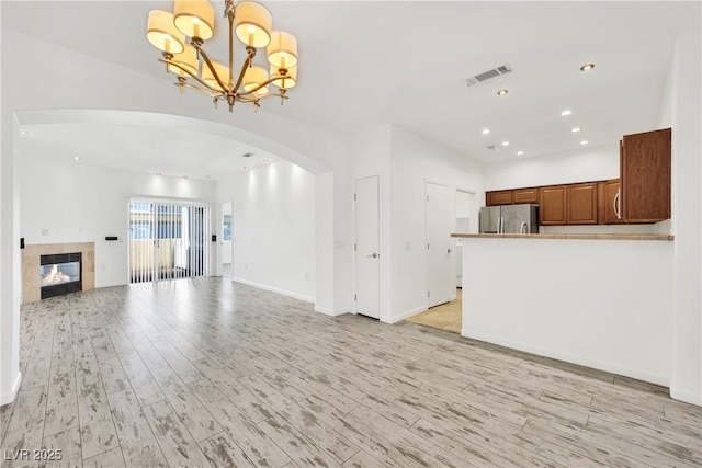 unfurnished living room featuring a tiled fireplace, an inviting chandelier, and light hardwood / wood-style flooring