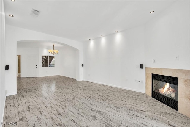 unfurnished living room with an inviting chandelier, a tile fireplace, and light wood-type flooring