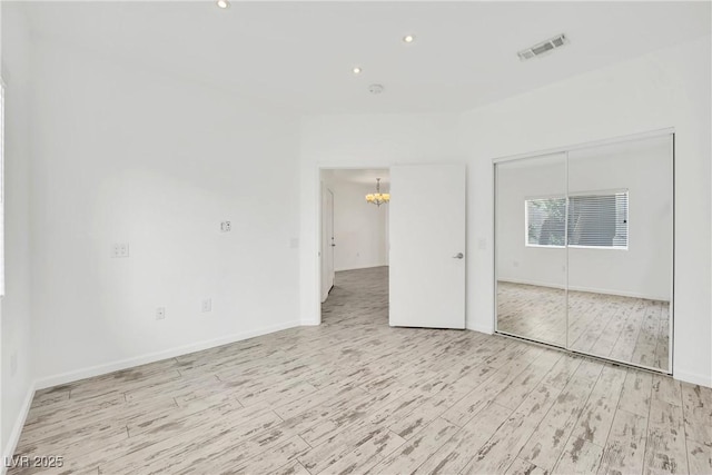 unfurnished room featuring an inviting chandelier and light wood-type flooring