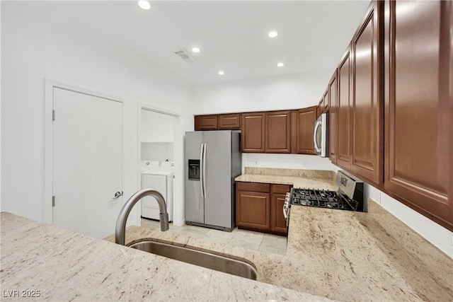 kitchen with appliances with stainless steel finishes, sink, light stone countertops, and washing machine and dryer