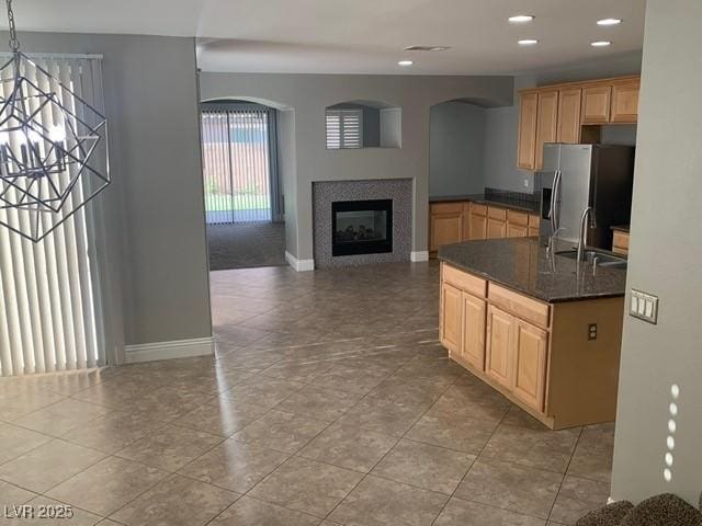 kitchen featuring stainless steel refrigerator with ice dispenser, sink, decorative light fixtures, dark stone counters, and a fireplace