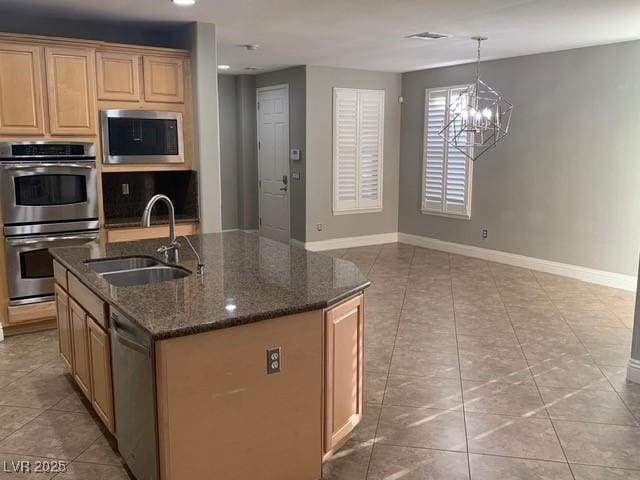 kitchen featuring appliances with stainless steel finishes, decorative light fixtures, sink, dark stone counters, and a center island with sink