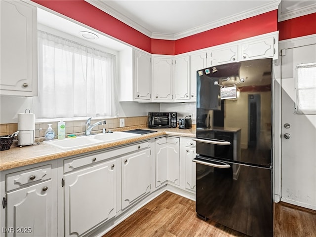 kitchen featuring white cabinetry, sink, light hardwood / wood-style flooring, and black fridge