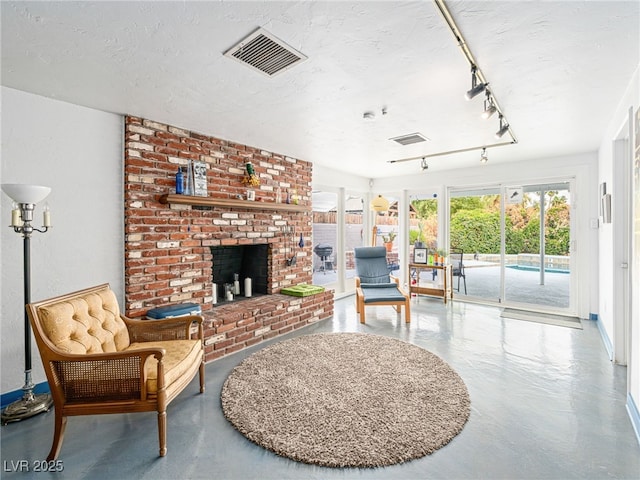 living room with a brick fireplace, track lighting, concrete floors, and a textured ceiling