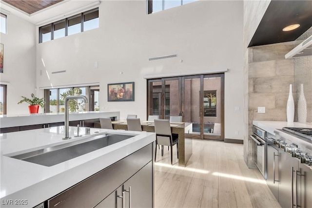 kitchen with sink, a towering ceiling, french doors, stainless steel oven, and light wood-type flooring