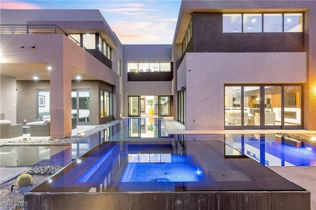 pool at dusk featuring an outdoor living space and an in ground hot tub