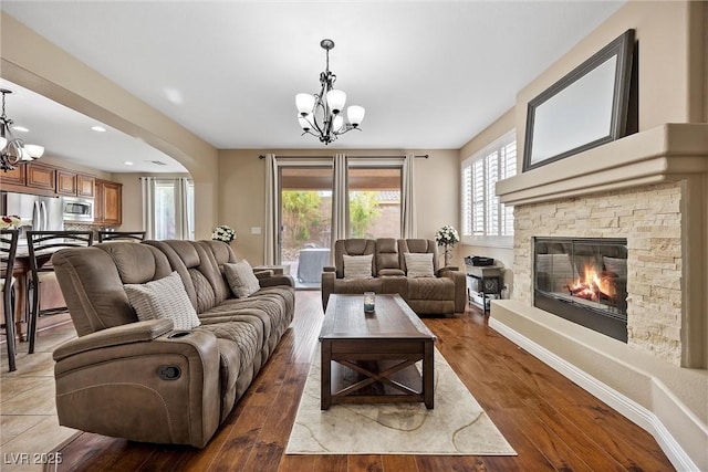 living room featuring a stone fireplace, a chandelier, and light hardwood / wood-style flooring