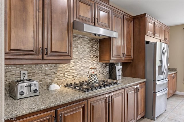 kitchen with stainless steel appliances, light tile patterned flooring, backsplash, and light stone counters