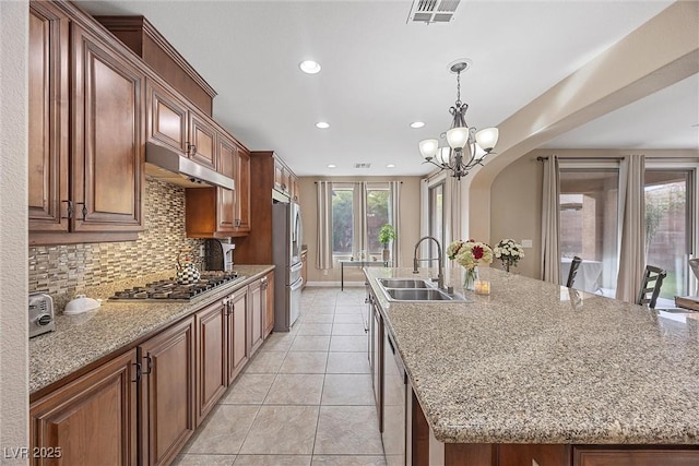 kitchen with sink, tasteful backsplash, a center island with sink, stainless steel appliances, and light stone countertops