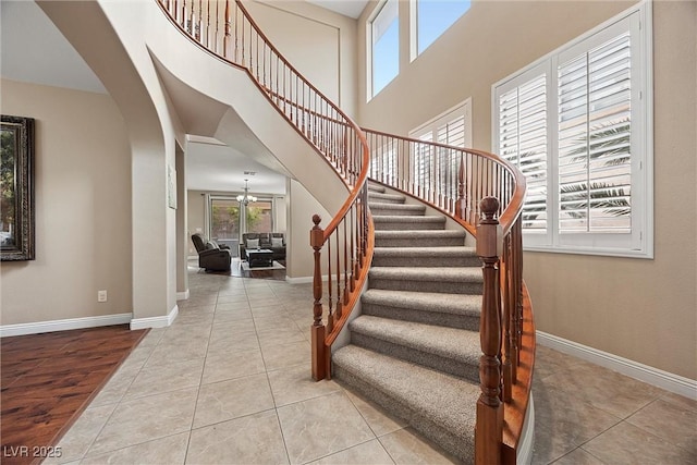 stairway featuring tile patterned flooring, a towering ceiling, and an inviting chandelier