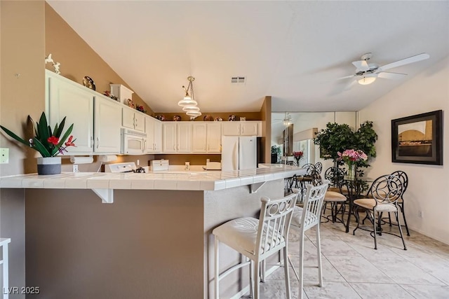 kitchen with white cabinetry, white appliances, tile counters, and a breakfast bar area