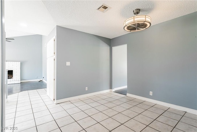 tiled empty room featuring ceiling fan, a brick fireplace, and a textured ceiling