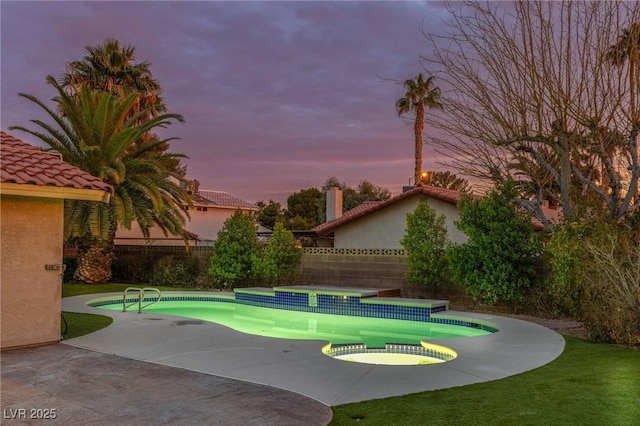 pool at dusk featuring an in ground hot tub and a patio area