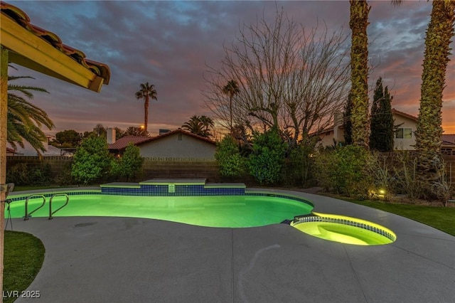 pool at dusk with an in ground hot tub