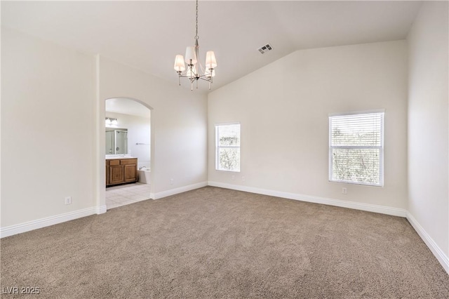 carpeted spare room featuring a notable chandelier and vaulted ceiling