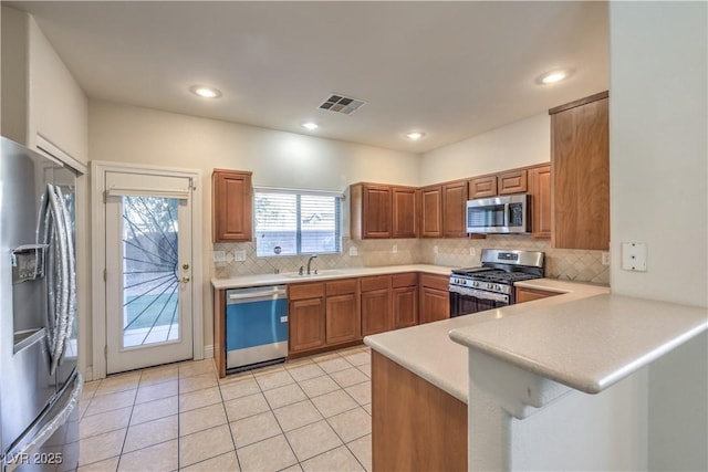 kitchen with appliances with stainless steel finishes, sink, decorative backsplash, light tile patterned floors, and kitchen peninsula