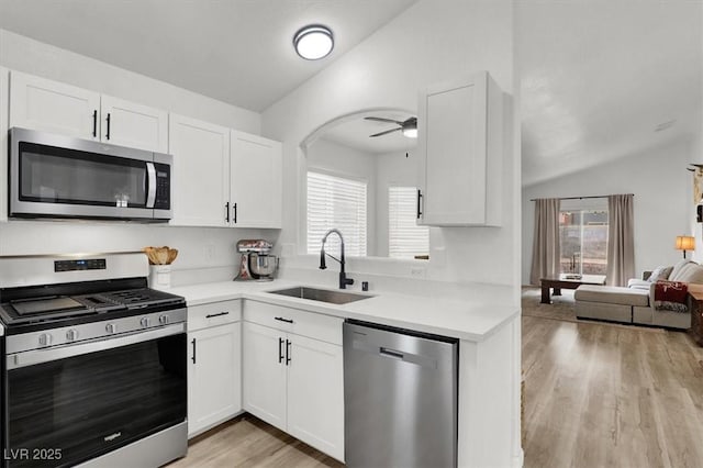 kitchen with sink, vaulted ceiling, ceiling fan, stainless steel appliances, and white cabinets