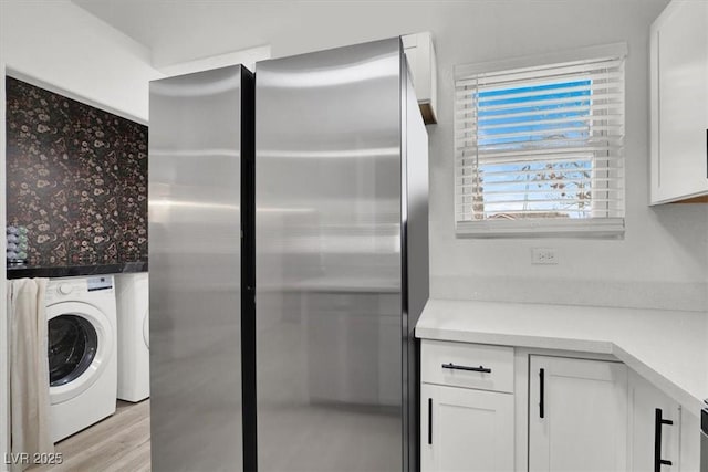 kitchen featuring washer / clothes dryer, white cabinetry, light wood-type flooring, and stainless steel refrigerator