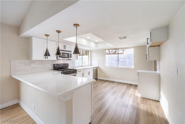 kitchen with white cabinetry, stainless steel appliances, decorative light fixtures, and kitchen peninsula