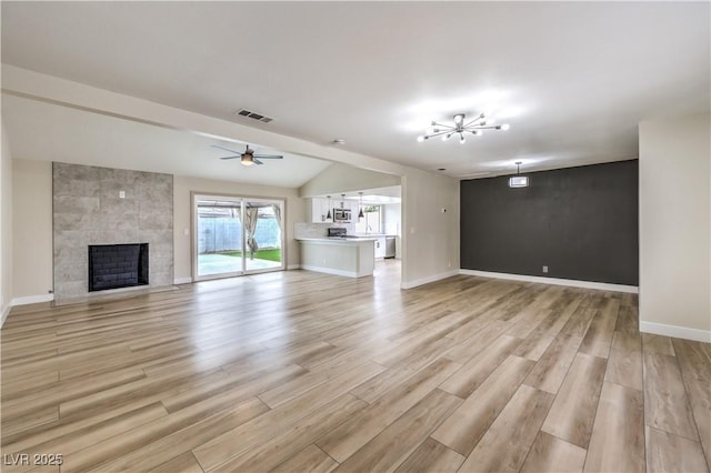 unfurnished living room with lofted ceiling, ceiling fan with notable chandelier, a fireplace, and light hardwood / wood-style floors