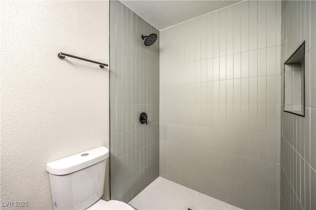 bathroom featuring a textured ceiling, toilet, and tiled shower