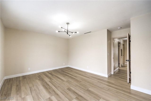 spare room with a notable chandelier and light hardwood / wood-style flooring