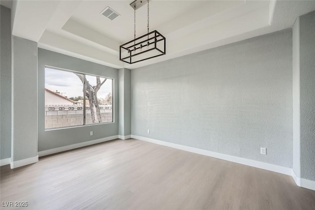 unfurnished dining area with wood-type flooring and a raised ceiling