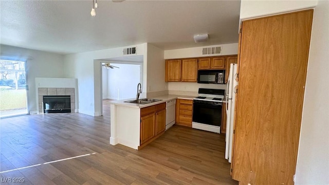 kitchen featuring sink, white appliances, a tile fireplace, ceiling fan, and hardwood / wood-style floors