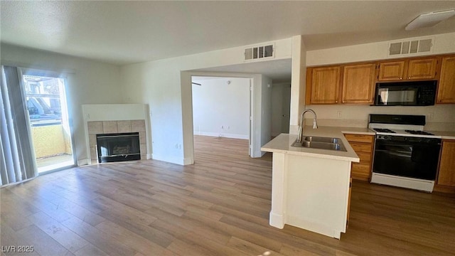 kitchen with sink, range with gas stovetop, kitchen peninsula, a fireplace, and light hardwood / wood-style floors