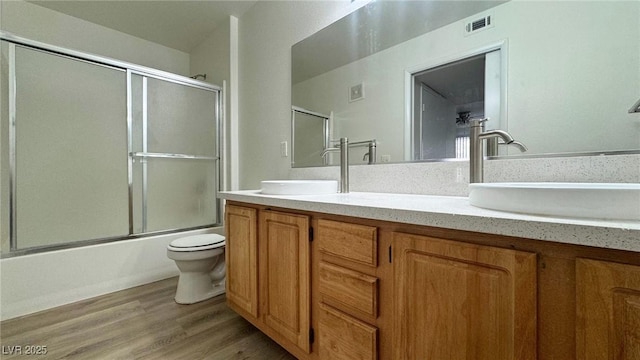 full bathroom featuring vanity, wood-type flooring, bath / shower combo with glass door, and toilet