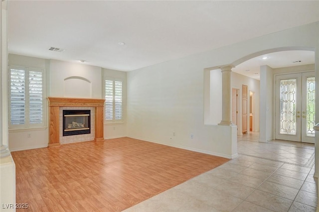 unfurnished living room featuring french doors, a tile fireplace, decorative columns, and light hardwood / wood-style flooring