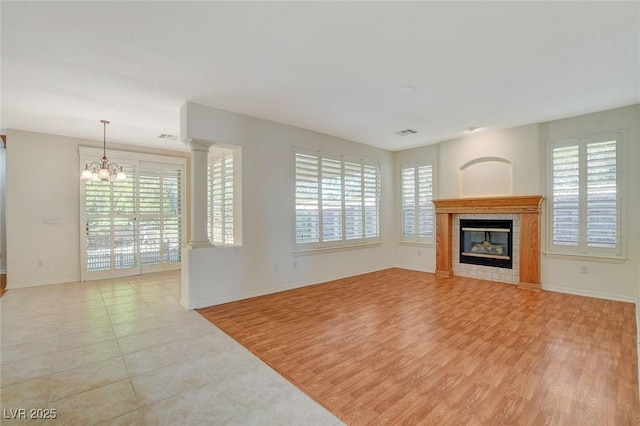 unfurnished living room featuring a tiled fireplace, a notable chandelier, and light hardwood / wood-style floors