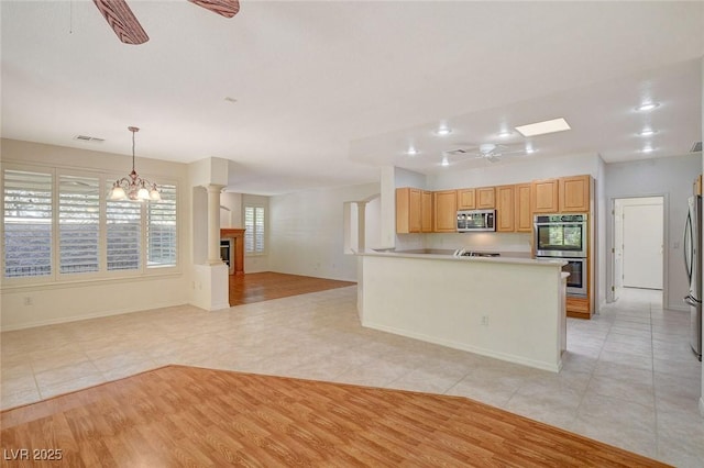 kitchen with ceiling fan with notable chandelier, hanging light fixtures, kitchen peninsula, stainless steel appliances, and light brown cabinets