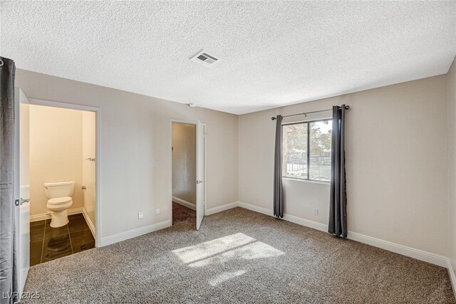 unfurnished bedroom featuring ensuite bath, carpet flooring, and a textured ceiling