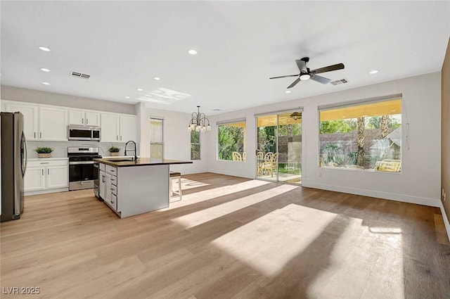 kitchen with appliances with stainless steel finishes, decorative light fixtures, sink, white cabinets, and a kitchen island with sink