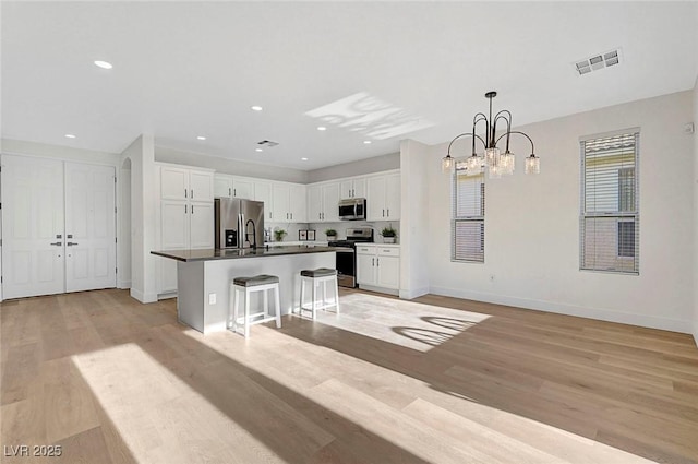 kitchen featuring a breakfast bar area, white cabinetry, light hardwood / wood-style flooring, an island with sink, and stainless steel appliances