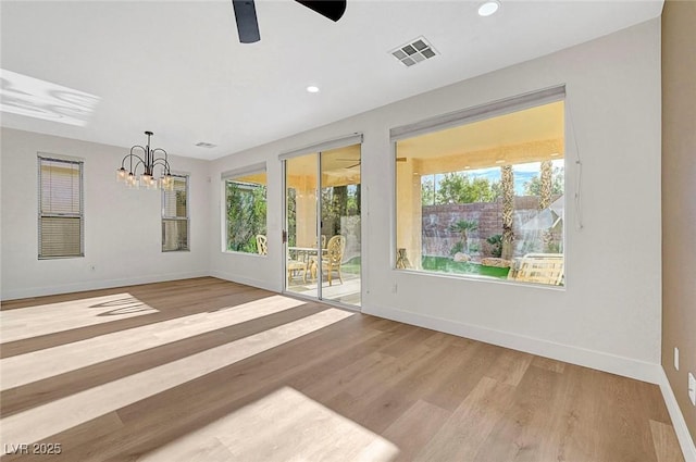 empty room with ceiling fan with notable chandelier and light hardwood / wood-style flooring