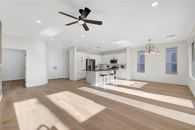 unfurnished living room featuring sink, ceiling fan with notable chandelier, and light wood-type flooring