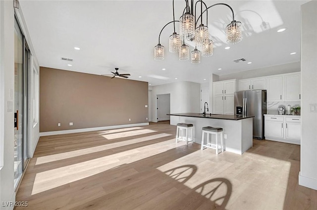 kitchen featuring hanging light fixtures, stainless steel fridge, a kitchen island with sink, light hardwood / wood-style floors, and white cabinets