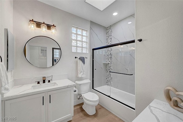 full bathroom featuring combined bath / shower with glass door, a skylight, wood-type flooring, vanity, and toilet