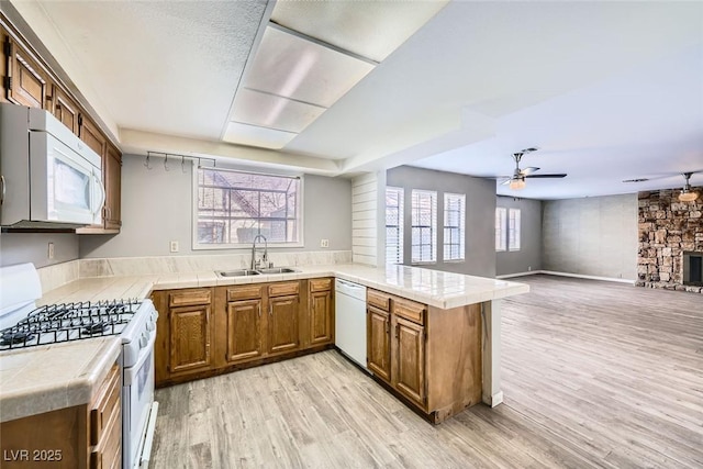 kitchen with sink, tile countertops, light wood-type flooring, kitchen peninsula, and white appliances