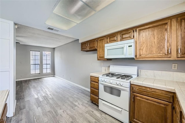 3954 Edgemoor Way, Las Vegas, NV 89121 - kitchen with white appliances, light wood finished floors, brown cabinetry, and tile counters