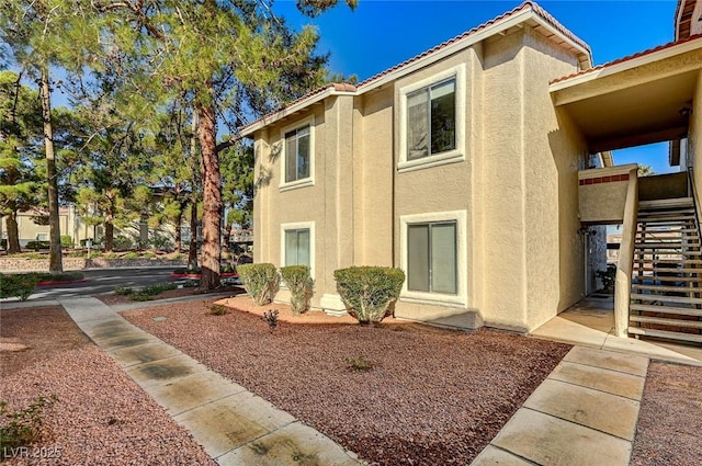 view of property exterior featuring a tiled roof, stairs, and stucco siding